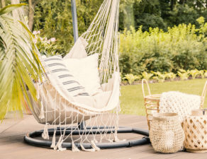 Lanterns and basket between rattan sofa and hammock with pillows in the garden.