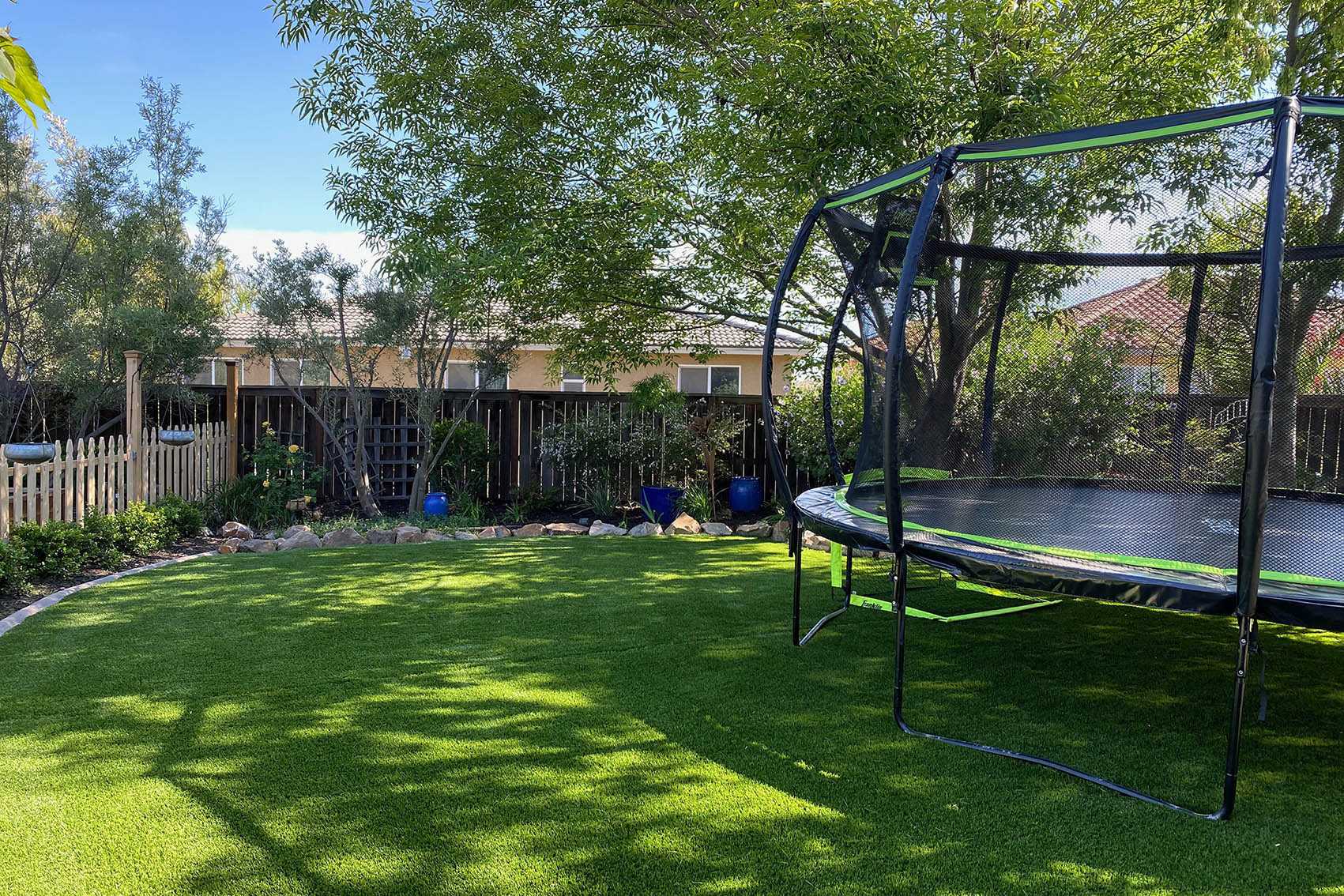 Trampoline in a residential back yard with artificial turf.
